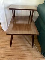 Front view of mid-century modern two-tier wood veneer side table showing brass capped legs and wear on edges