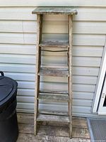 Full view of old wooden ladder standing upright showing all rungs and weathered paint.