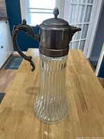 Full view of vintage glass pitcher/carafe with silver plated lid and handle on wooden surface