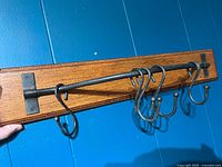 Front angle view of the wall hanging pot rack showing wood grain MDF and 6 metal hooks on black metal bar.