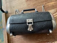 Front angled view showing detailed tooling on leather, steel clasp, and handle.