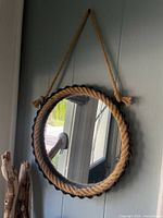 Front view of round hanging mirror showing grey fluted metal frame and thick natural rope border and hanging rope loop.