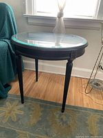 Side view of the black wood circular side table with beveled glass top, showing the four legs and decorative accents.