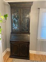 Front view of dark brown wood Hooker Furniture secretary hutch with glass doors on top and closed cabinet doors at bottom, showing golden decorative accents and wood grain.