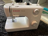 White Singer Prelude sewing machine with dials and controls visible.