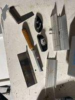 Photo showing two mitre boxes, two saws, and a steel square on white surface