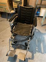 Front view of the black folding transport wheelchair showing padded seat, backrest, armrests, and foot plates.