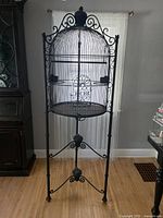 Front view of entire black iron birdcage on tripod stand with dome top