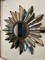 Front view of the vintage art deco sunburst mirror showing circular center mirror and multiple mirrored beams radiating outward, some with smoky tint and decorative ball ends.
