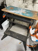 Workbench with metal frame and worn wooden top with paint marks, black foot pedal visible
