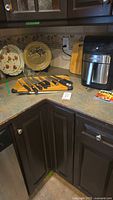 Corner countertop showing seven kitchen knives on a holder, wooden cutting board, two decorative ceramic pie plates, and airfryer.