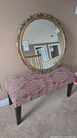 Photo showing the bench with red/beige patterned upholstery and dark legs, with the oval gold framed mirror on top.