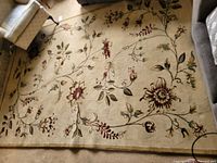 Full view of beige floral area rug in living room setting showing large floral motifs with red, green, and brown tones.
