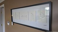 Framed art hung on beige wall with six drawings and Picasso signature.
