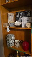 Image of curated shelf with cherub stone vase, red owl figurine, mug, plate, inspirational and decorative plaques, and framed art.