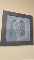 Full view of the framed Buddha wall art hung on a beige wall.