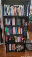 Full view of black shelving unit filled with various books on five shelves