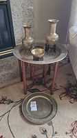 Brass charger topped wooden folding leg table next to a stone fireplace, with brass vases and dishes arranged on the tray surface