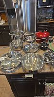 Cuisinart and other cookware items arranged on a kitchen counter, including pots, pans, lids and a red Dutch oven.