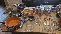 Wide photo showing various cookware pots, pans, wire rack, and cutlery arranged on a kitchen counter.