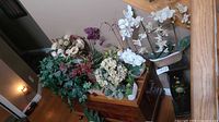 Photo of a group of faux flower arrangements including orchids and mixed flowers on a wooden surface.
