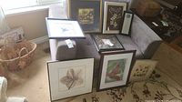 Seven framed wall art pieces arranged on a couch and floor near window, showing various botanical and nature-themed prints and different frame styles.