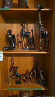 Shelf with multiple giraffe figurines of different materials and sizes, including a tall painted wooden giraffe, black metallic ones, and painted natural wooden giraffes.