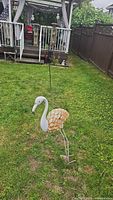 Full view of metal flamingo lawn ornament in grass near porch, showing general size and placement