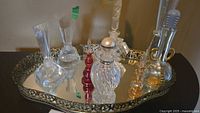 Six glass scent bottles with various shapes and stoppers arranged on an ornate mirrored tray with filigree edge