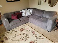 Overall view of the grey fabric sectional sofa in an L-shape arrangement, showing cushions and pillows.