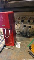 Red Sodastream machine next to glass bottles and drinking glasses on kitchen counter