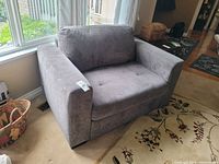 Gray twin-sized sleeper chair positioned near a window. Shows wide armrests, tufted seat and plush back cushion.