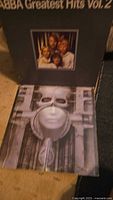Vinyl record album covers showing ABBA Greatest Hits Vol. 2 and a biomechanical face album.