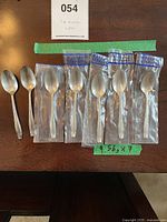 Seven Wallace sterling silver demitasse spoons laid out on a table, five in original plastic packaging, two unwrapped, with a tag noting 9.56g each.