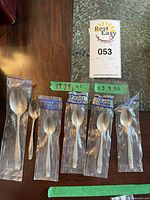 Six Wallace sterling silver spoons displayed on wood surface, five demitasse spoons mostly in original packaging, one teaspoon loose.