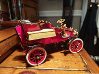 Side view of red 1903 Ford Model A diecast car with black seats and gold-tone details placed on wooden surface.