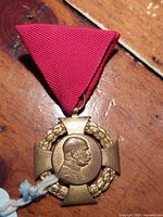 Front view of the antique Austrian 1848-1908 Jubilee Cross medal showing the bust of Emperor Franz Joseph I within a laurel wreath over a bronze cross suspended from a triangular red ribbon.
