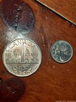 Two coins on wooden surface: a large Canada Bicentennial Big Nickel 5 cents coin dated 1751-1951 and a smaller Canadian 5 cents coin.