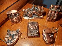 Overview photo showing all six copper lighters with distinct graphic designs on a wooden surface.