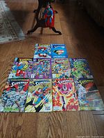 Photo showing the hand crafted painted Superman marionette alongside 10 vintage Superman comic books from the 1990s laid out on wooden floor.