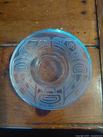 Top-down view of clear circular glass tea light holder showing detailed etched Thunderbird design and artist signature 'Wade Baker'