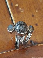 Front angled view of the ring on a wooden surface showcasing Yooperlite center stone and oval Labradorite side stones with hammered band detail.