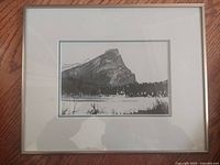 Framed vintage monochrome photograph of Mt Rundle with double mat and glass covering, showing mountain and surrounding forest and fields.