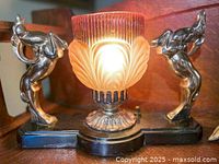 Front angle showing lamp lit with frosted amber and cream glass shade, two stylized gazelle figurines on black base with gold-tone accents.