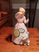 View of Royal Doulton figurine 'Reward' in pink dress with small dog, showing front and side angles.