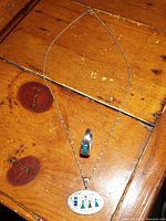 Sterling silver chain with oval white pendant showing colorful tribal summer solstice scene with four stylized figures and symbols, and a silver ring with pyramid-shaped blue lapis lazuli stone.