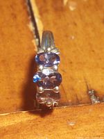 Close-up front view of the sterling silver ring with three vertically aligned oval purple gemstones on a textured natural brown background.