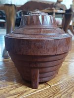 Front view of rounded Bakelite humidor showing geometric carved details, ridged lid, and footed base.