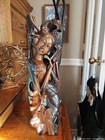 Front view of the carved wooden female figure with birds on head and shoulder, sitting on a wooden surface with other decor items in background.