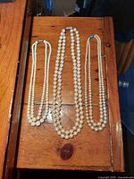 Three vintage double-string pearl necklaces displayed flat on wooden surface, showing varying pearl sizes and clasp details.